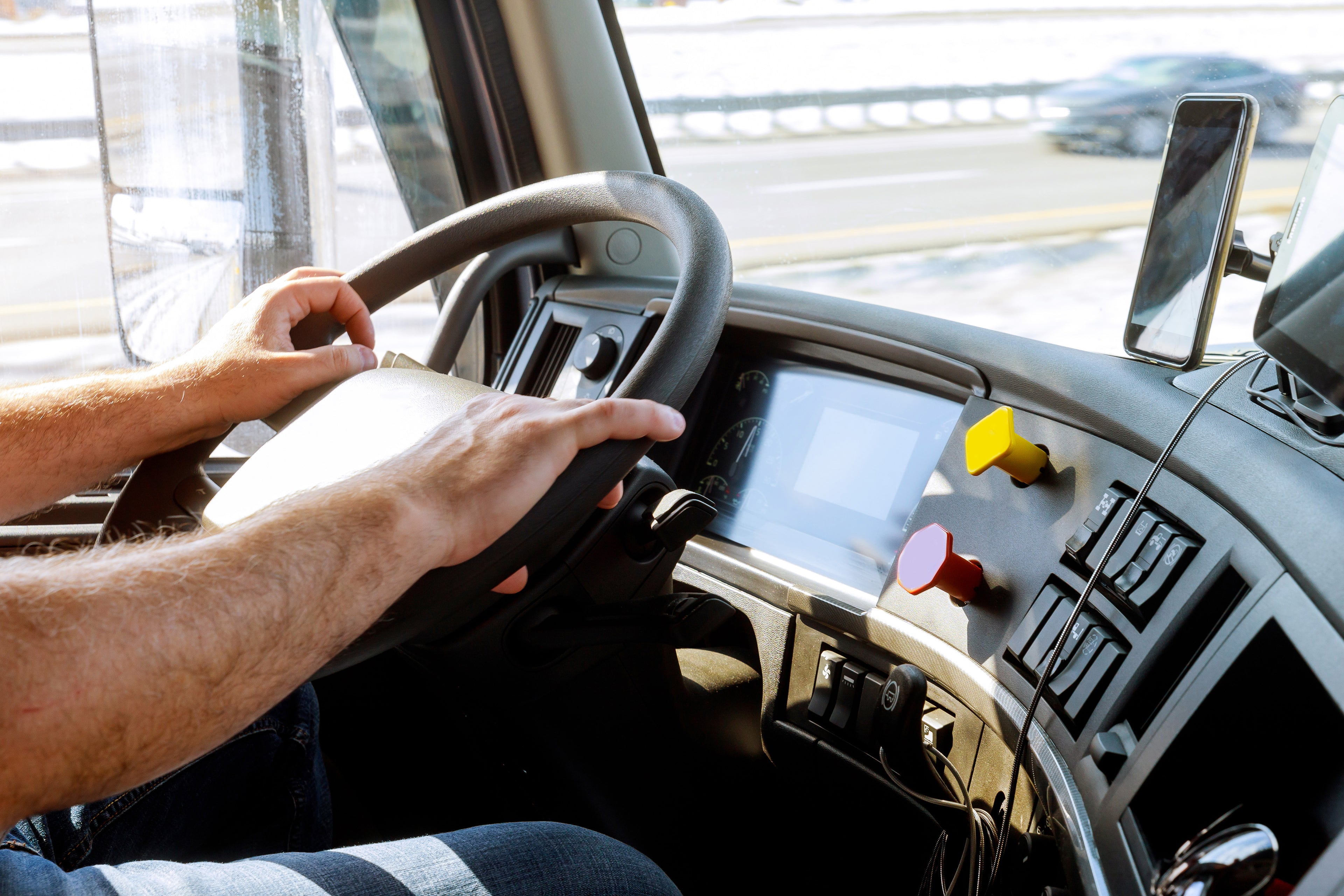 Sun shines on the hands and steering wheel in the truck cabin of a delivery truck driver on the job driving on the highway.