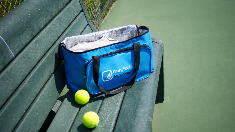 Blue thermal-insulated storage bag with Krazy Kool Tech logo on a green bench next to tennis balls