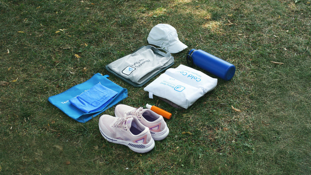 Collection of runners gear including a Krazy Kool Tech System, breathable cycling hat, running shoes, water bottle, sunscreen, and bags laid out on grass