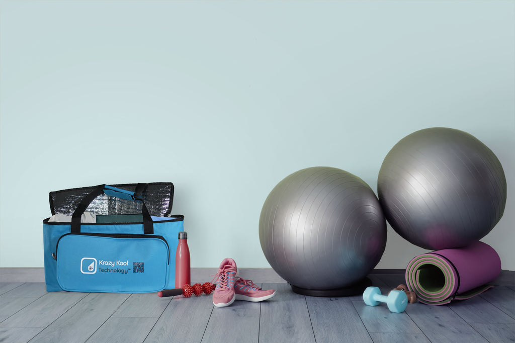 Gym equipment including a blue bag, water bottle, sneakers, exercise balls, and a yoga mat on a wooden floor.