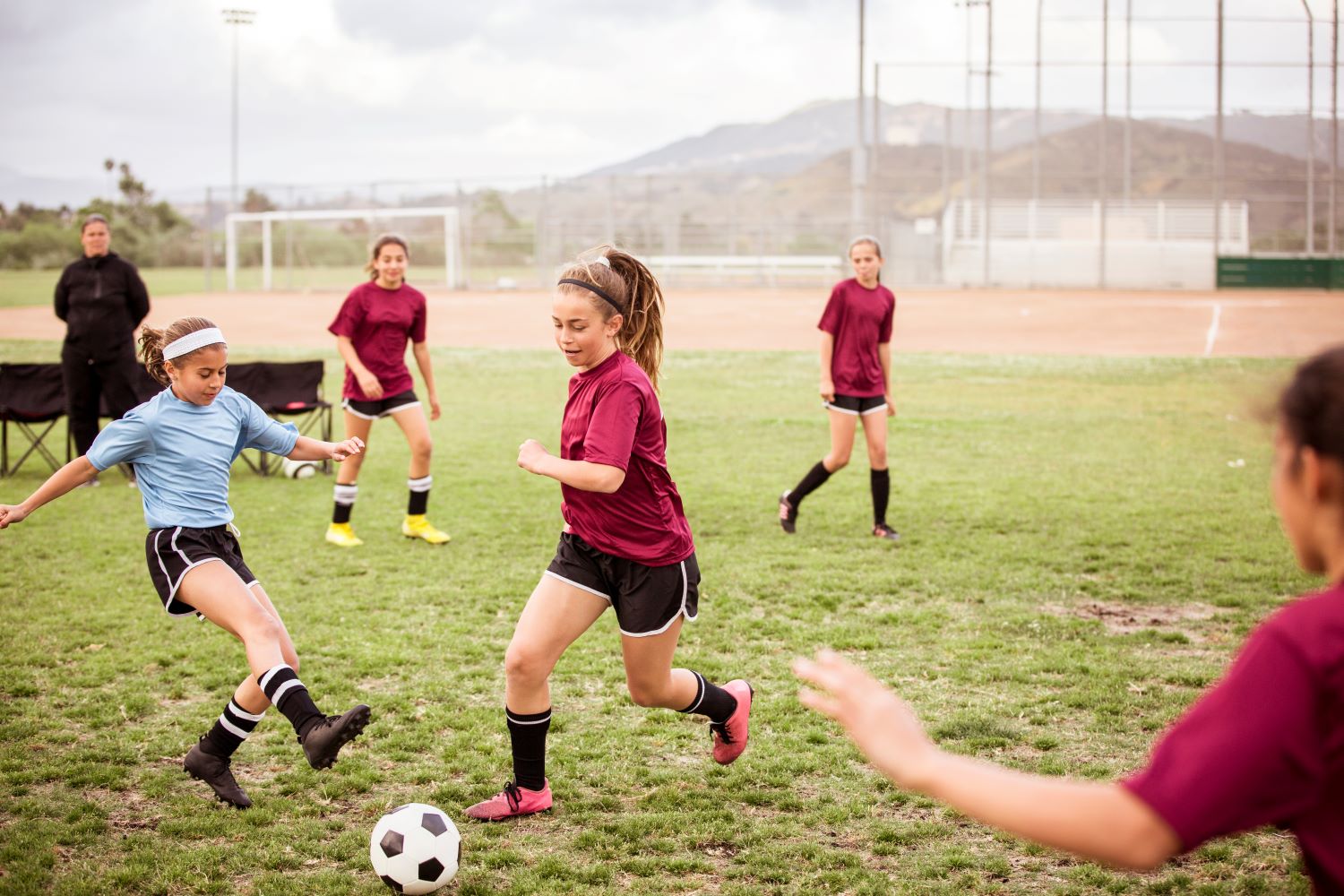 Girls playing soccer on a grass field with Australian mountains in the background