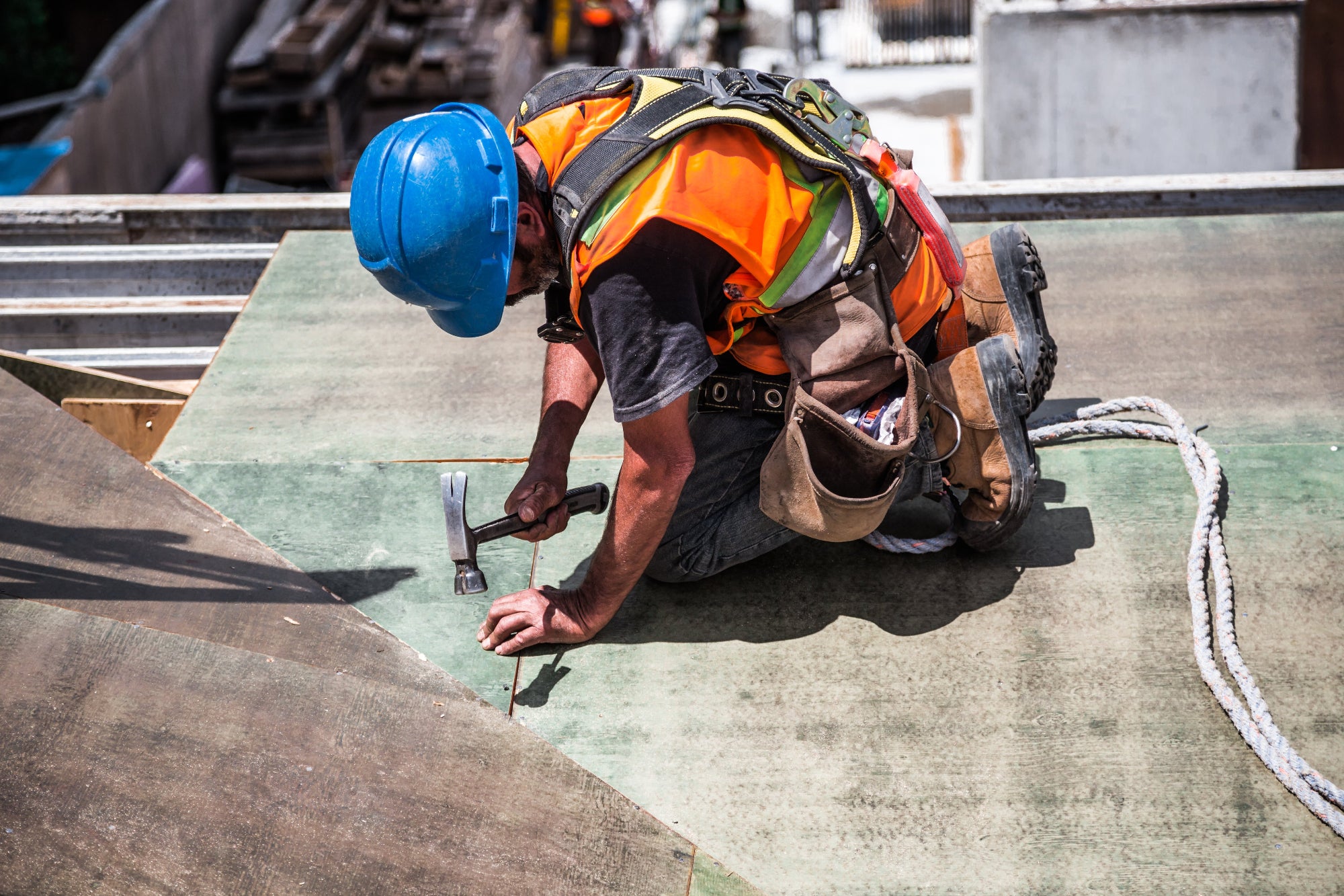construction worker wearing safe protective equipment outside building and hammering a roof in the outdoor sun and heat